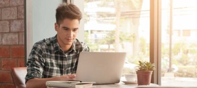 Young man using laptop with tablet and pen on wooden table